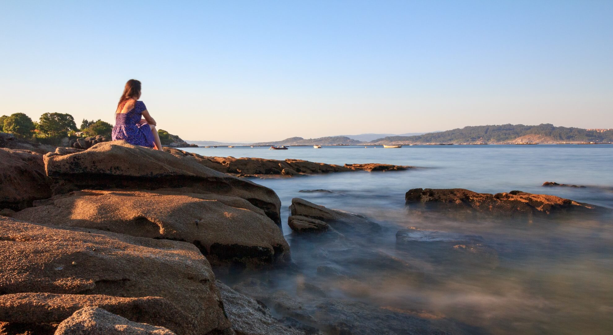 henkilö istuu kivellä ja katsoo merta